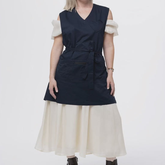 woman in a navy apron turning to face the back and show the back of the full coverage apron 